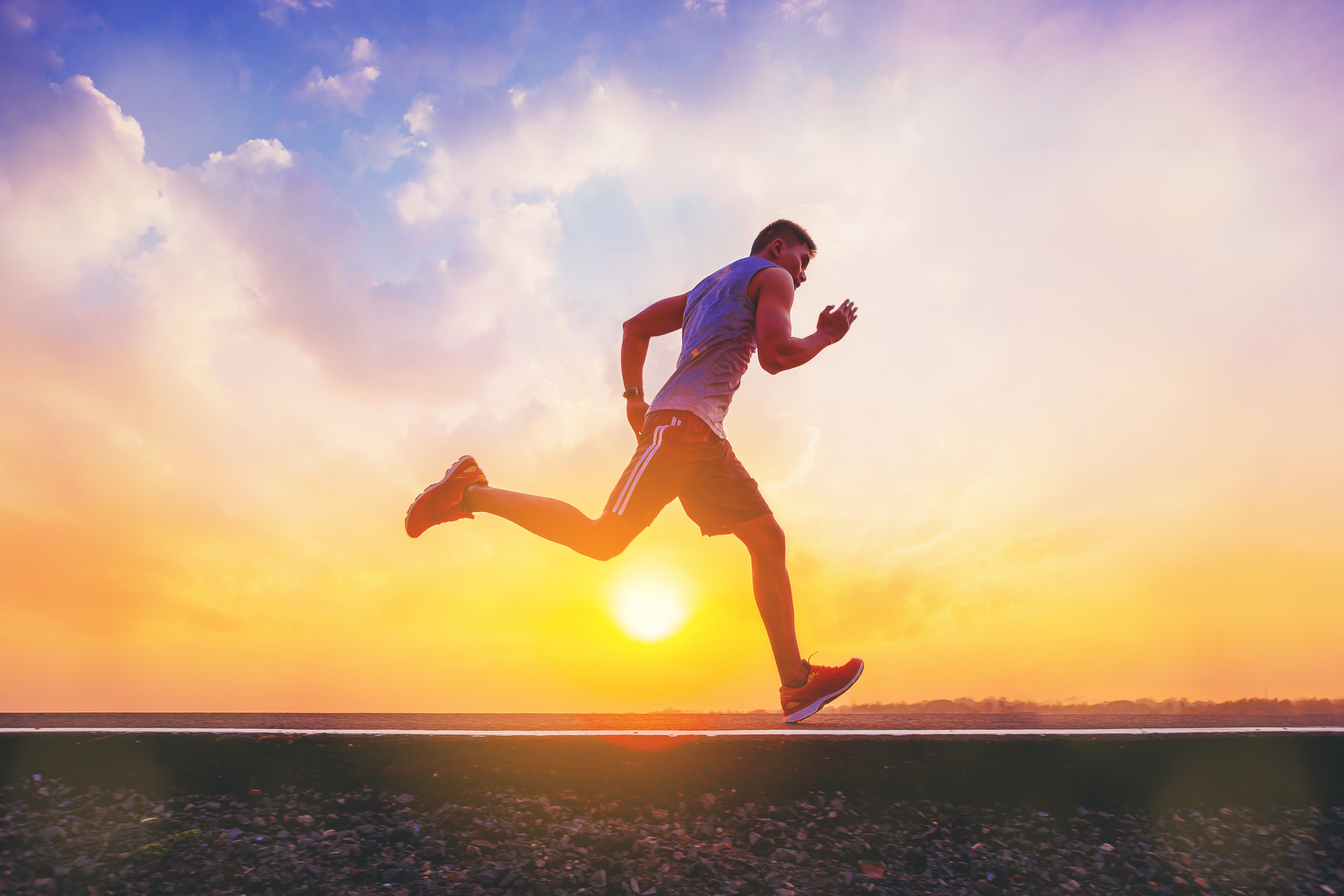 Silhouette of man running sprinting on road. Fit male fitness runner during outdoor workout with sunset background